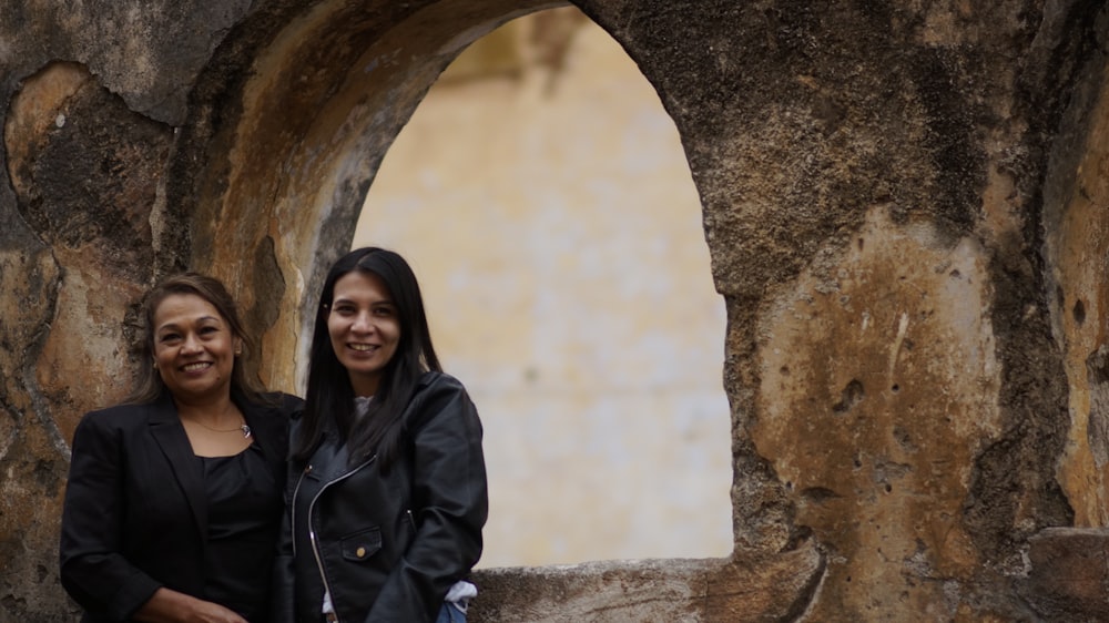 a couple of women smiling in front of a rock cave