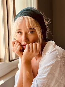 A serene, softly lit photo of karimah montshá sitting by a window with a notebook, lost in thought.