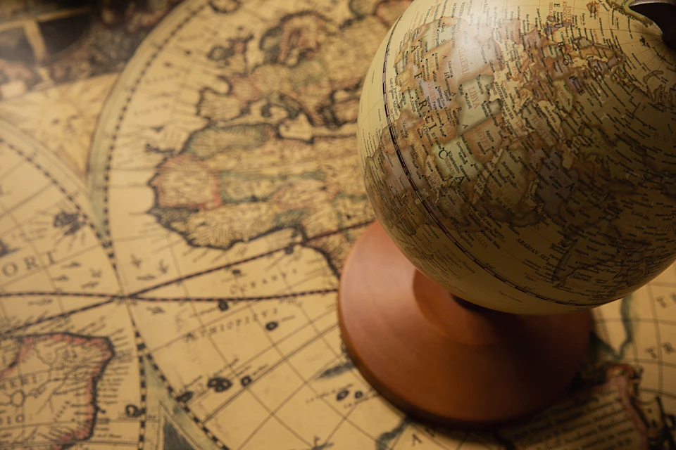 The image shows a vintage globe with a brown wooden base and a white top, resting on a map that is slightly tilted to the left. The map features various countries and bodies of water, providing geographical context for the globe's location.