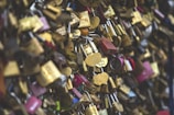 A dense collection of variously colored padlocks attached to a structure, symbolic of love and commitment. Some locks are engraved with names and dates, including heart-shaped ones. The scene is vibrant with an assortment of locks, indicating a popular site for couples.