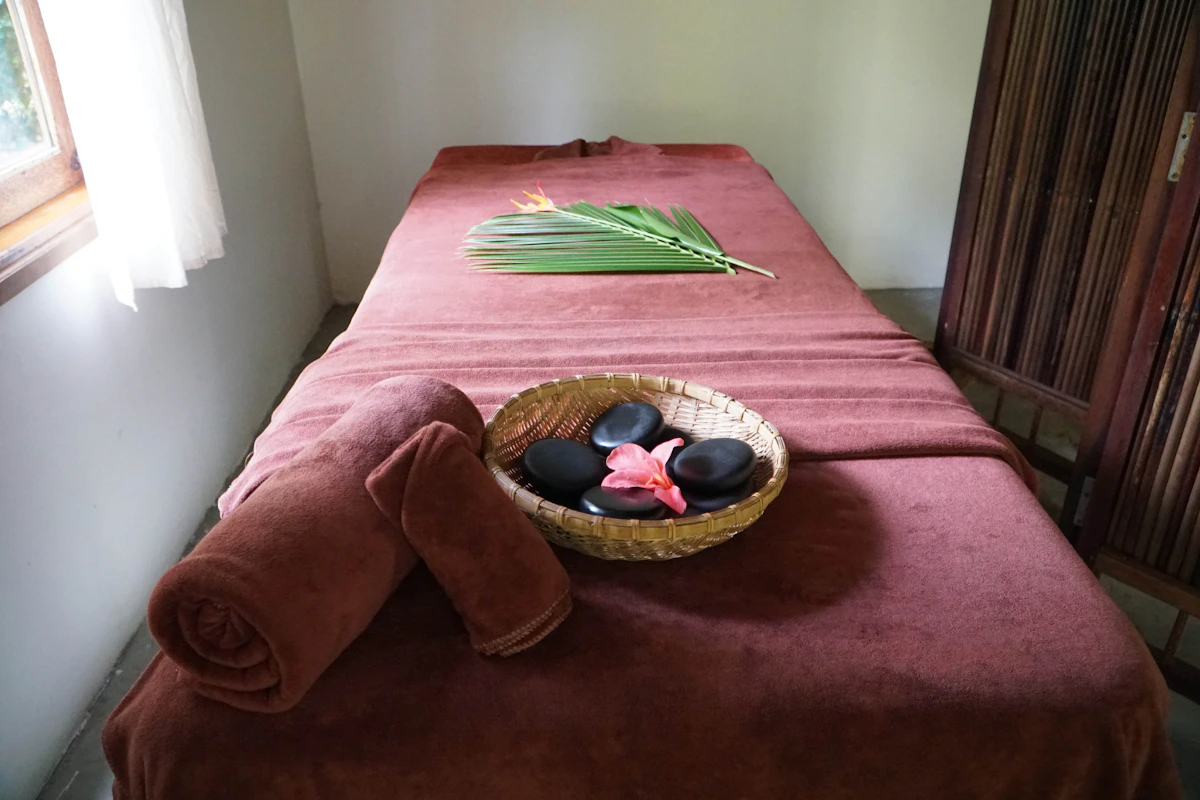 A made-up massage table with rolled towels, hot stones and a sprig of eucalyptus