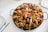 A large pan filled with vibrant paella, featuring cooked prawns, mussels, clams, and vegetables mixed with saffron-infused rice. The seafood is arranged on top, creating an appealing and appetizing look. The dish is placed on a white textured tablecloth, with plates and cutlery neatly arranged around it.