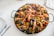 A large pan filled with vibrant paella, featuring cooked prawns, mussels, clams, and vegetables mixed with saffron-infused rice. The seafood is arranged on top, creating an appealing and appetizing look. The dish is placed on a white textured tablecloth, with plates and cutlery neatly arranged around it.