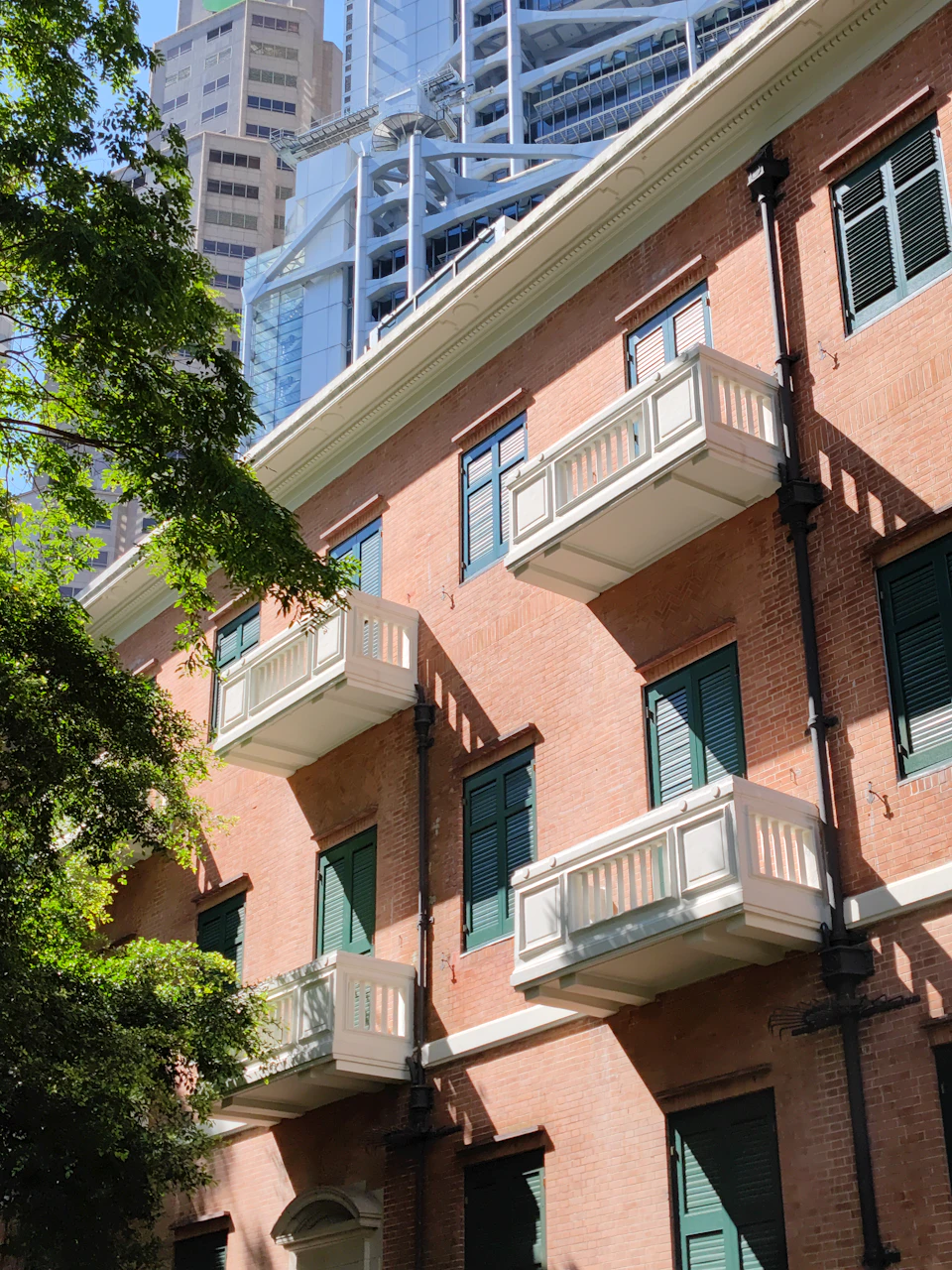 Tall red brick building with white trim and green shutters in urban cityscape