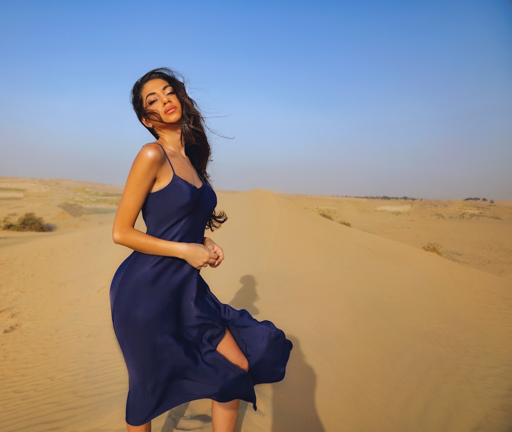 a woman in a blue dress standing in the sand