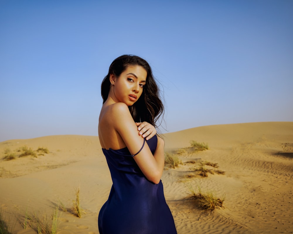 a woman in a blue dress standing in a sandy area
