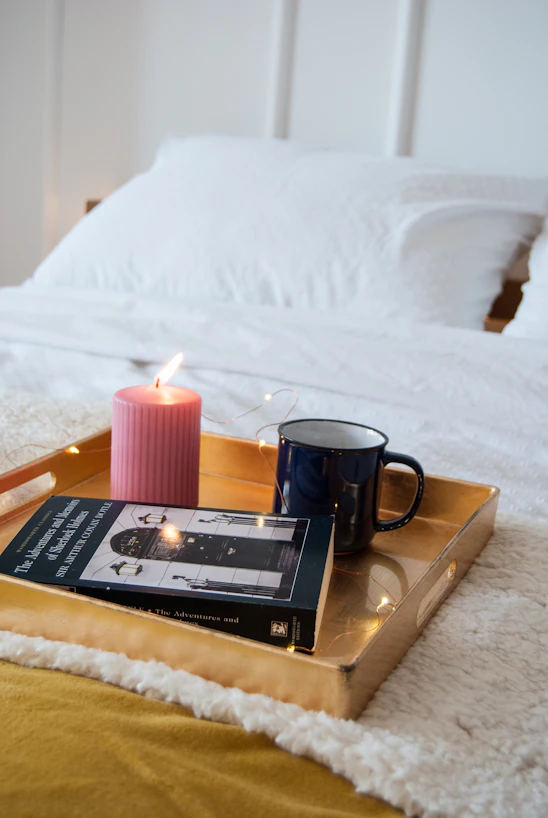 A pastel-hued cozy corner with a plush blanket, journal, candle, and a cup of matcha on a wooden tray.