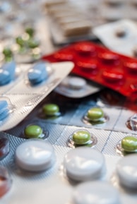 Various blister packs containing pills are displayed, featuring different colors such as white, green, blue, and red. The image focuses on the texture and layout of the blister packs scattered around.