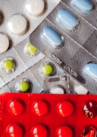 Several blister packs containing different types of pills. There are white, blue, and green pills in metallic silver packaging, and red pills in a bold red packaging.