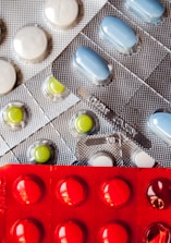 Several blister packs containing different types of pills. There are white, blue, and green pills in metallic silver packaging, and red pills in a bold red packaging.
