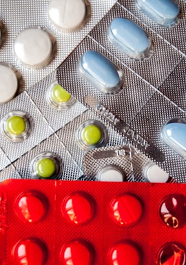 Several blister packs containing different types of pills. There are white, blue, and green pills in metallic silver packaging, and red pills in a bold red packaging.