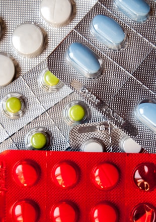 Several blister packs containing different types of pills. There are white, blue, and green pills in metallic silver packaging, and red pills in a bold red packaging.