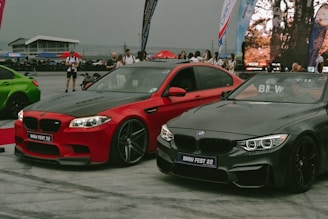 Two sleek BMW cars parked side by side at an outdoor car event, surrounded by people and banners with a modern, sporty atmosphere.