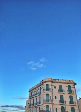 A vintage-style hotel building with several stories, adorned with green shutters and balconies. The structure is situated under a clear blue sky, giving it a picturesque and serene appearance.