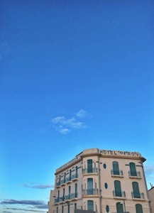 A vintage-style hotel building with several stories, adorned with green shutters and balconies. The structure is situated under a clear blue sky, giving it a picturesque and serene appearance.