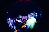 A vibrant concert scene captured with a fisheye lens, showing a musician playing a guitar on stage, surrounded by a lively audience under dynamic lighting.