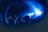 In a dimly lit indoor setting, silhouettes of people are visible, with their arms raised, seemingly enjoying a lively music event. The scene is bathed in vibrant blue lighting, creating an energetic and immersive atmosphere.