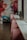 A stylish interior space with a row of pink chairs lined up against a long, white countertop. A vibrant mural featuring large floral designs with shades of red, pink, and blue adorns the wall. Potted plants are placed on the counter near large windows that let in soft natural light.