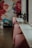 A stylish interior space with a row of pink chairs lined up against a long, white countertop. A vibrant mural featuring large floral designs with shades of red, pink, and blue adorns the wall. Potted plants are placed on the counter near large windows that let in soft natural light.