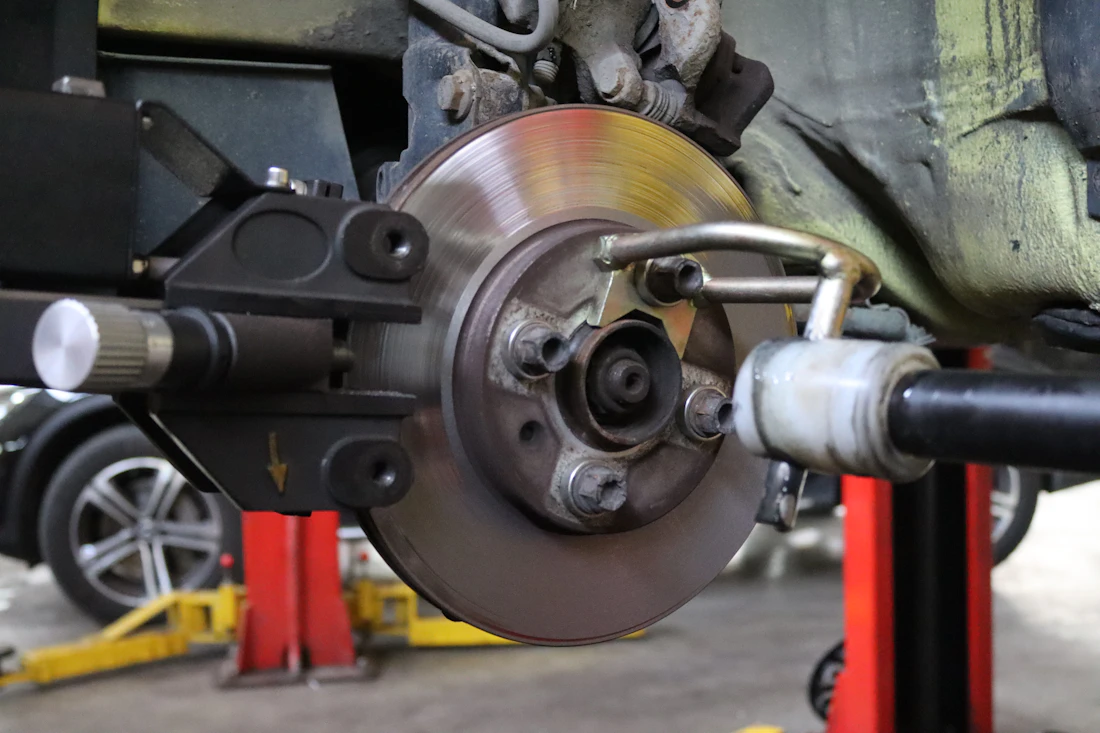 A brake rotor and hub exposed on a vehicle raised on a shop lift with red jack stands