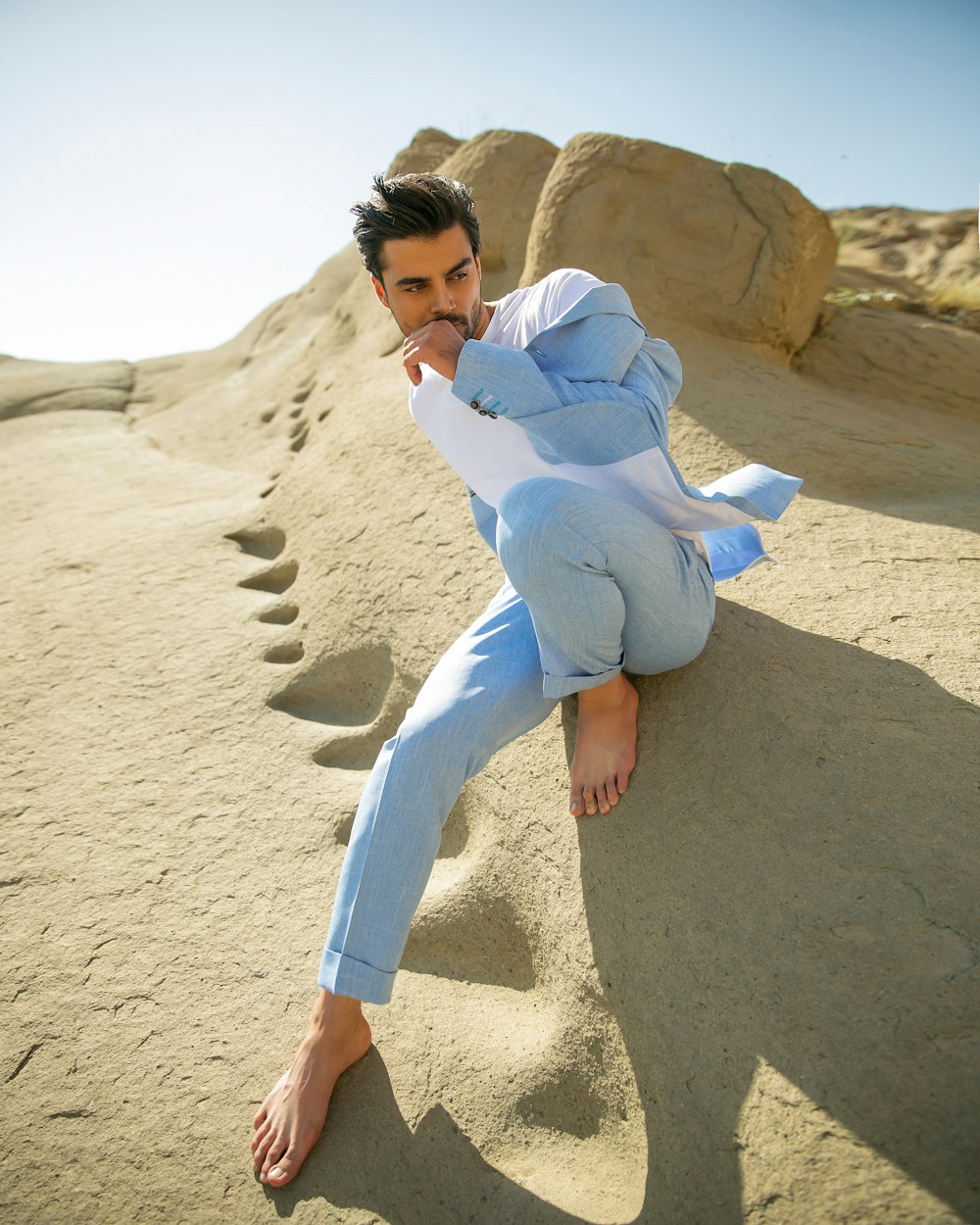 uma pessoa em uma camisa azul e jeans sentada em uma praia de areia