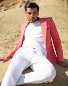A man dressed in a light coral shirt and beige pants, with subtle sea-inspired jewelry, posing near underwater-themed decorations.