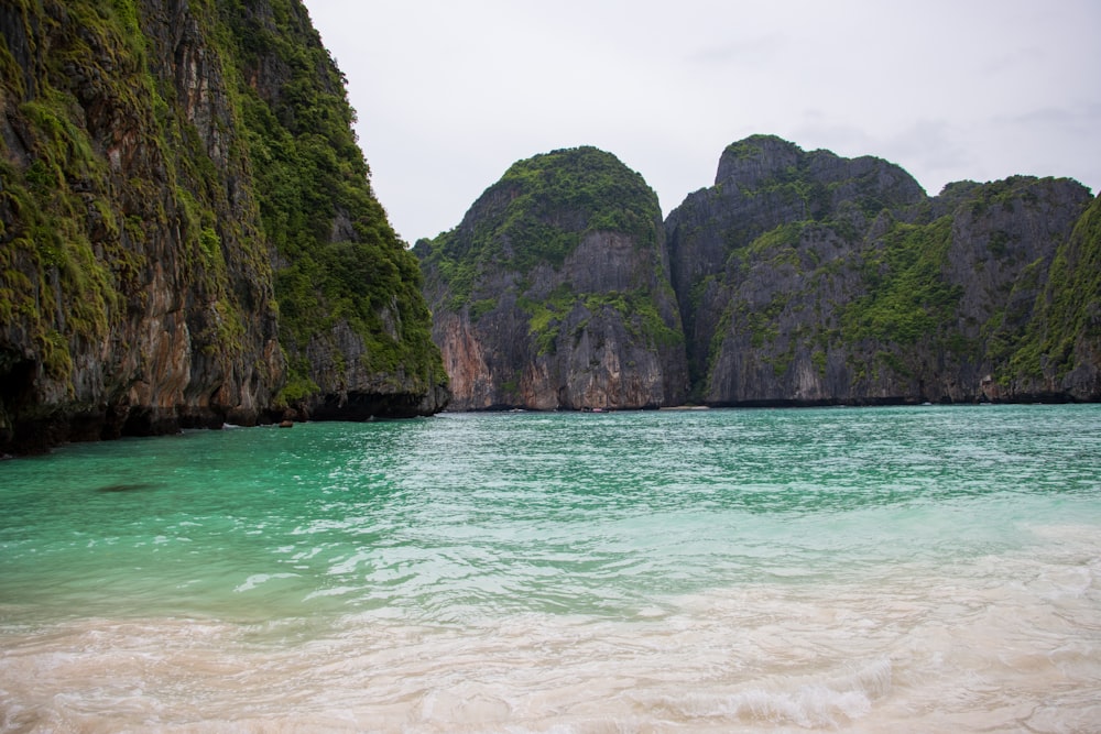 a body of water with a rocky cliff in the background with Phi Phi Islands in the background