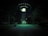A dark outdoor setting illuminated by a large, glowing UFO hovering above. Three figures stand in its beam of light, surrounded by trees and parked cars. The scene is surreal and otherworldly, with an eerie green hue cast over the landscape.