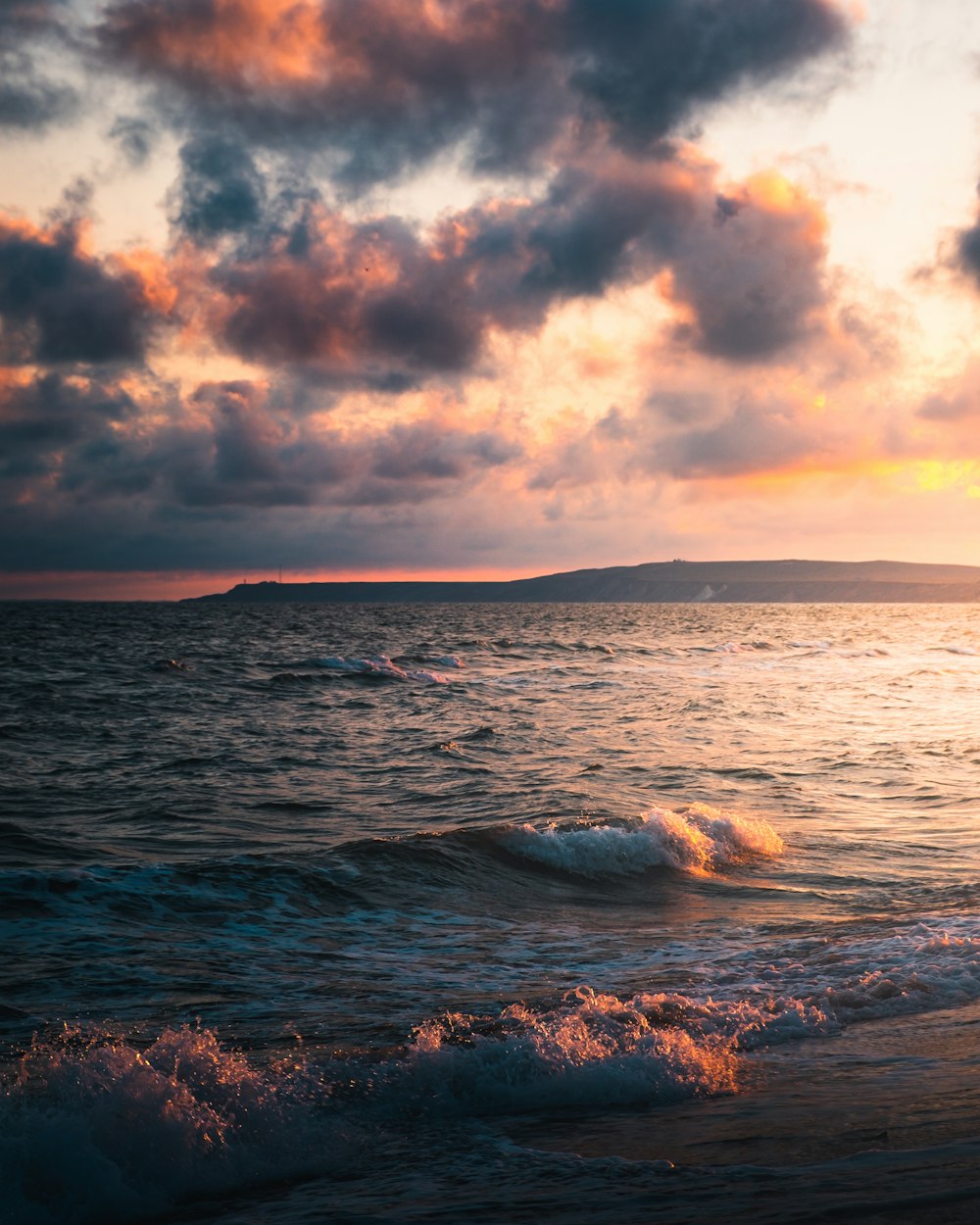 a body of water with waves and clouds above it