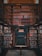 A richly wooden-paneled library alcove filled with shelves of colorful books. The scene is symmetrical, with a central green door labeled as Deck 46, indicating telephone books and city directories. The shelves surround the door, climbing up towards a mezzanine level, and are densely packed with books of various sizes and colors.
