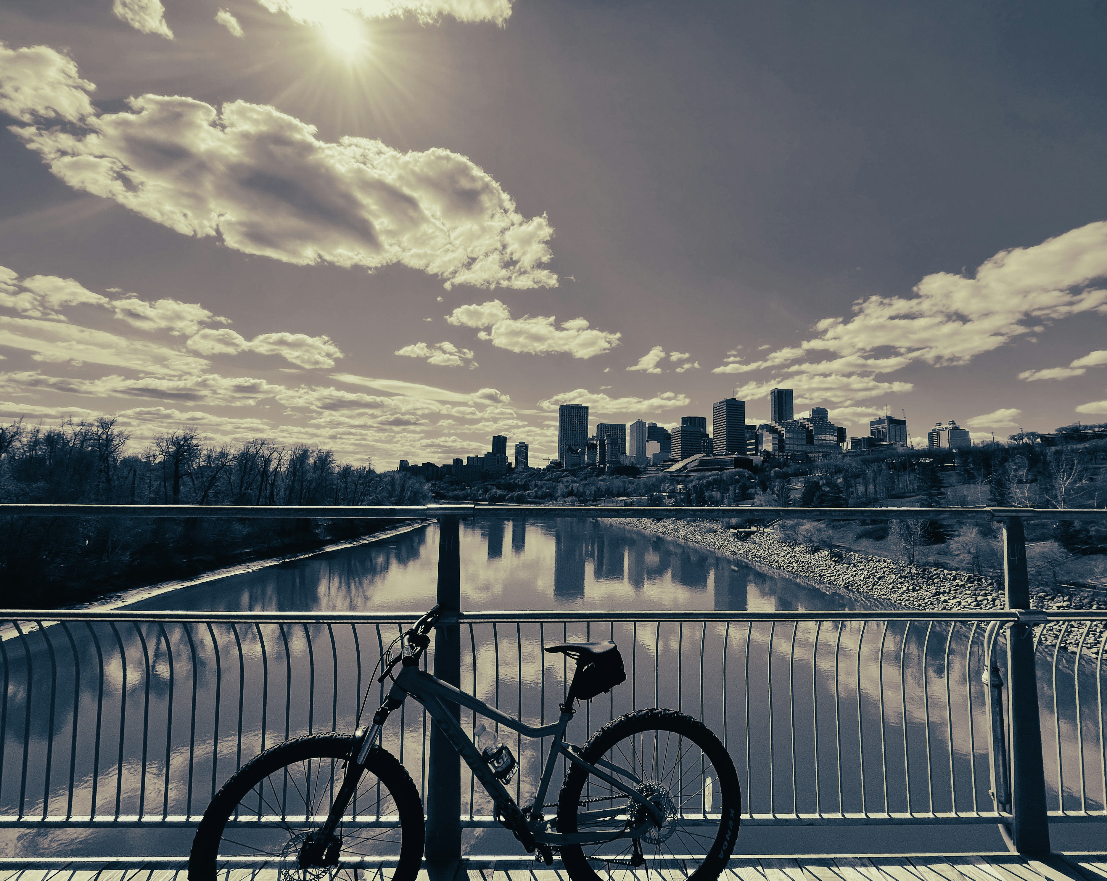 a bicycle parked on a bridge over a body of water with a city in the background