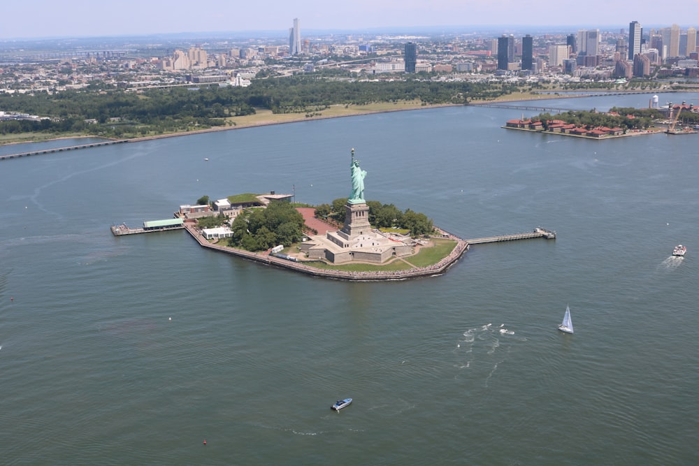 uma estátua em uma ilha com um corpo de água e Ellis Island no fundo