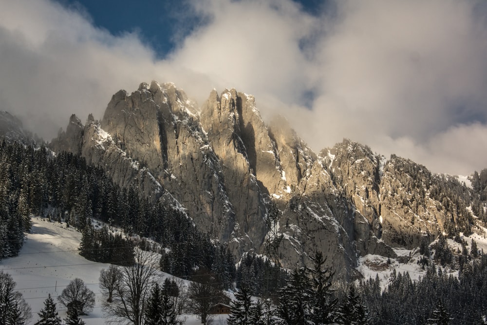 a snowy mountain with trees and clouds