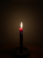 A glowing red candle surrounded by rose petals and softly flickering incense smoke.