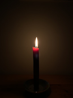 A glowing red candle surrounded by rose petals and softly flickering incense smoke.