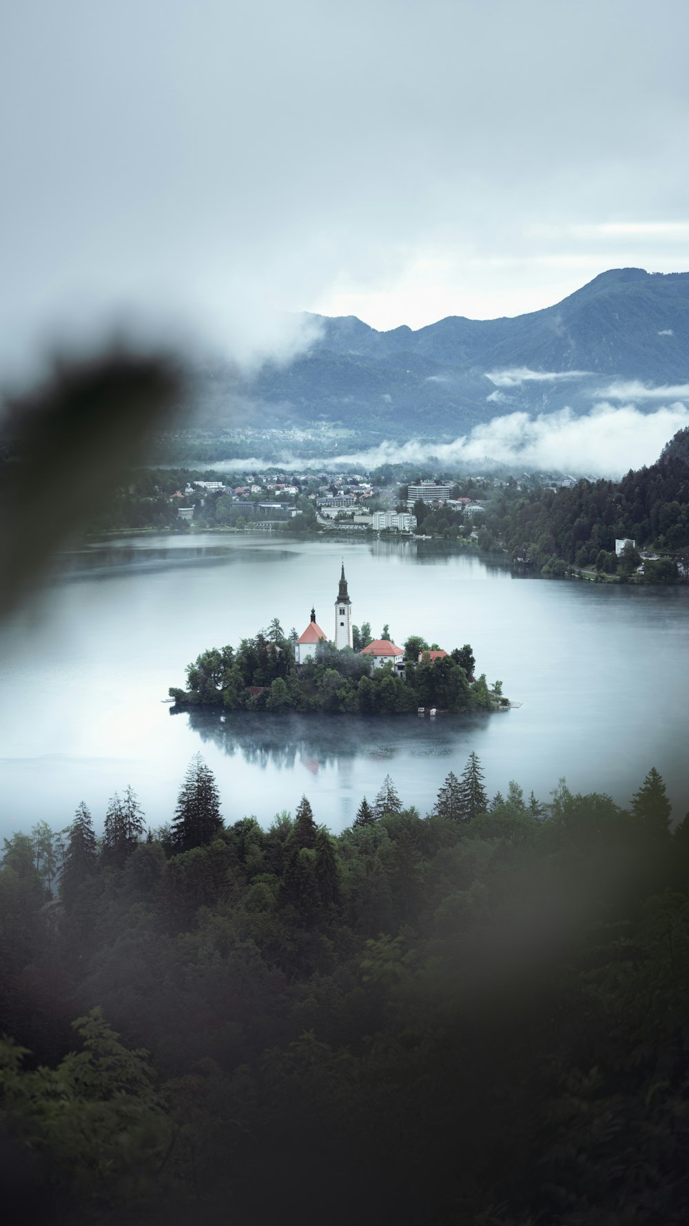 a small island with a building on it surrounded by trees and mountains