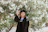 Portrait of a smiling alumnus in school uniform standing by the historic oak tree on campus.