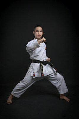 Adult karate student in a white gi and black belt in a front stance, Adult Elite karate class