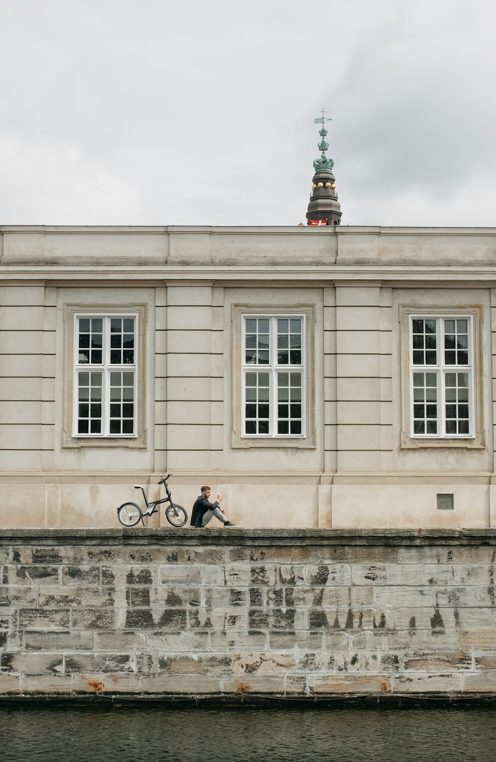 a person sitting on a wall next to a building with a bicycle