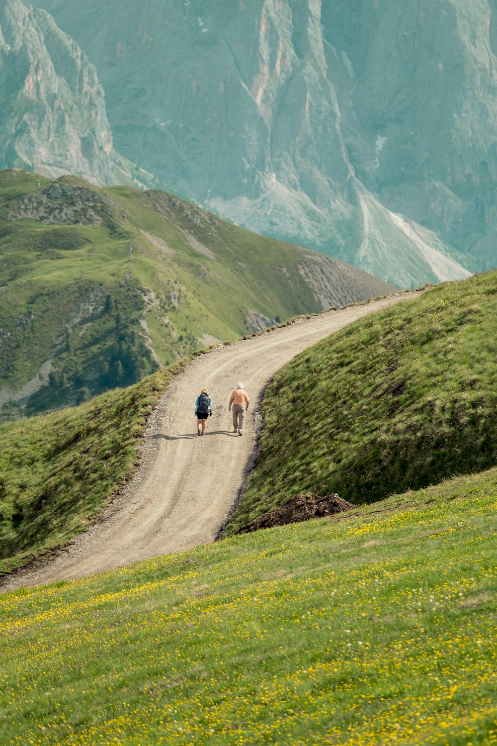 two people walking on a dirt road in a valley with mountains