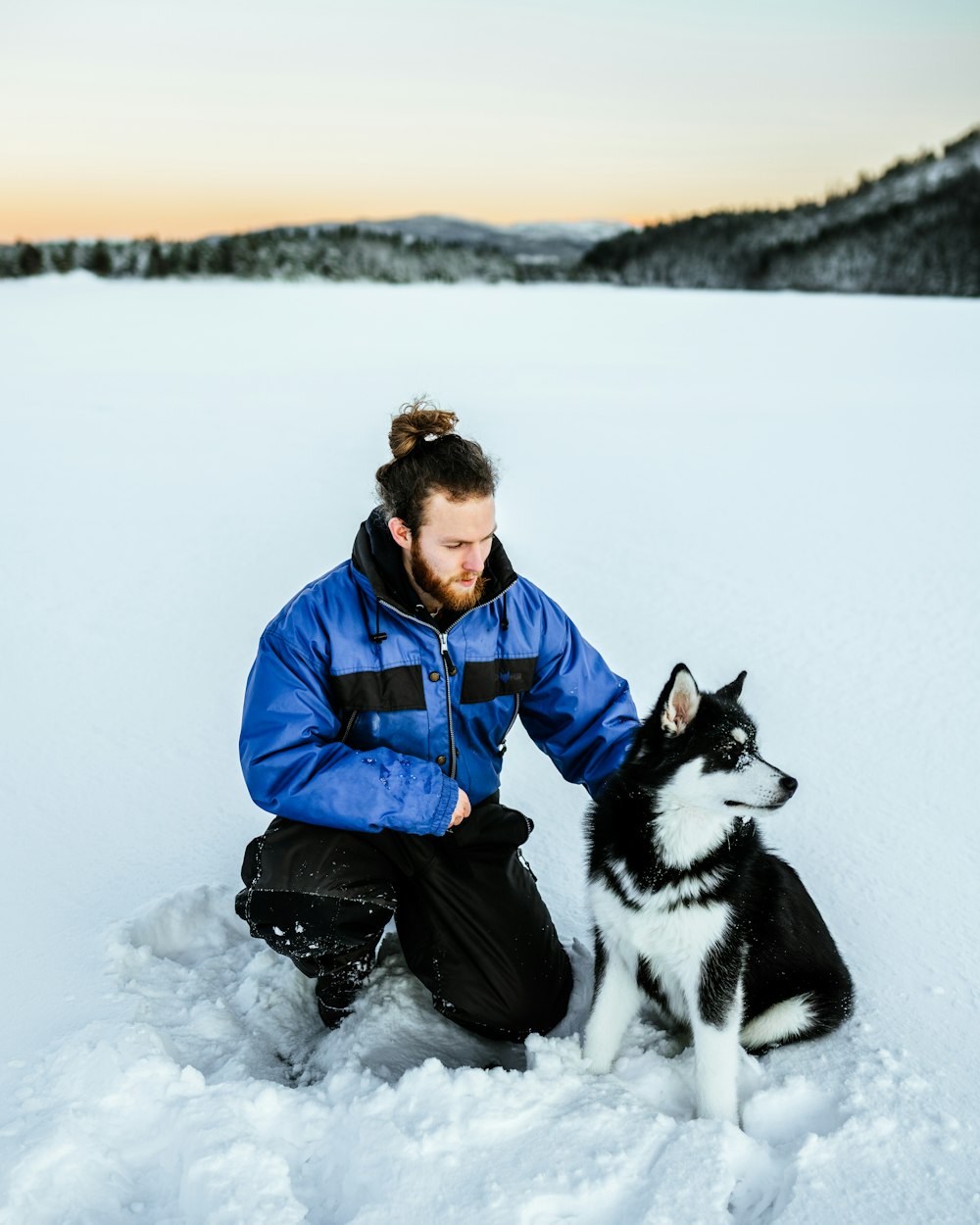 a man kneeling in snow with a dog