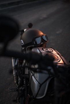 A worn steel helmet resting on a vintage motorcycle seat under dim garage lighting.