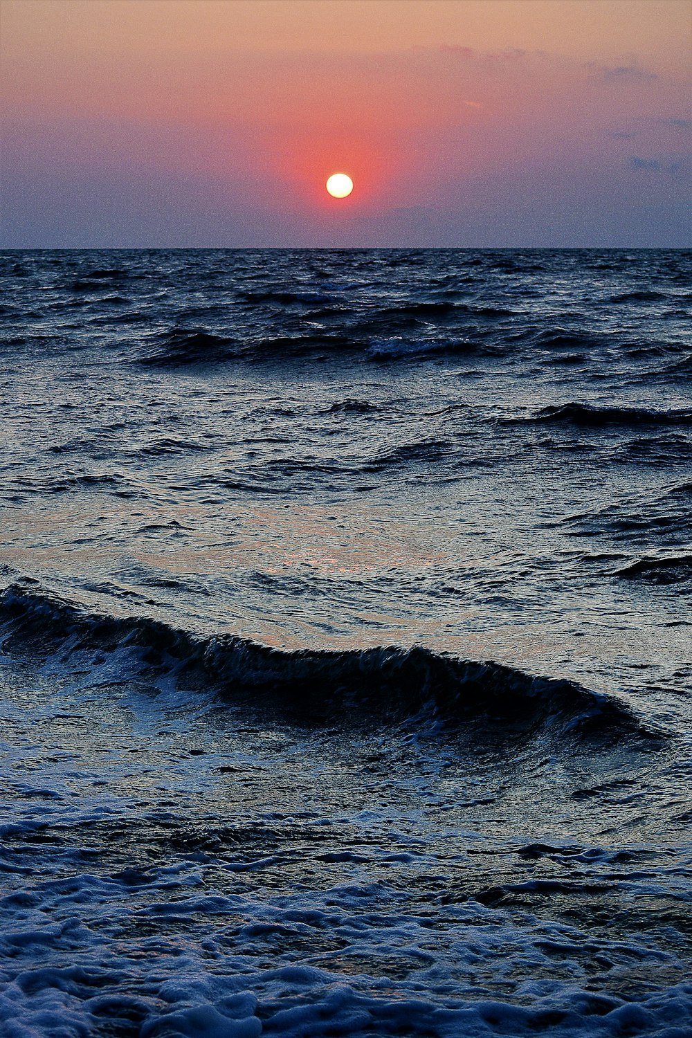 un plan d’eau avec des vagues et un coucher de soleil en arrière-plan