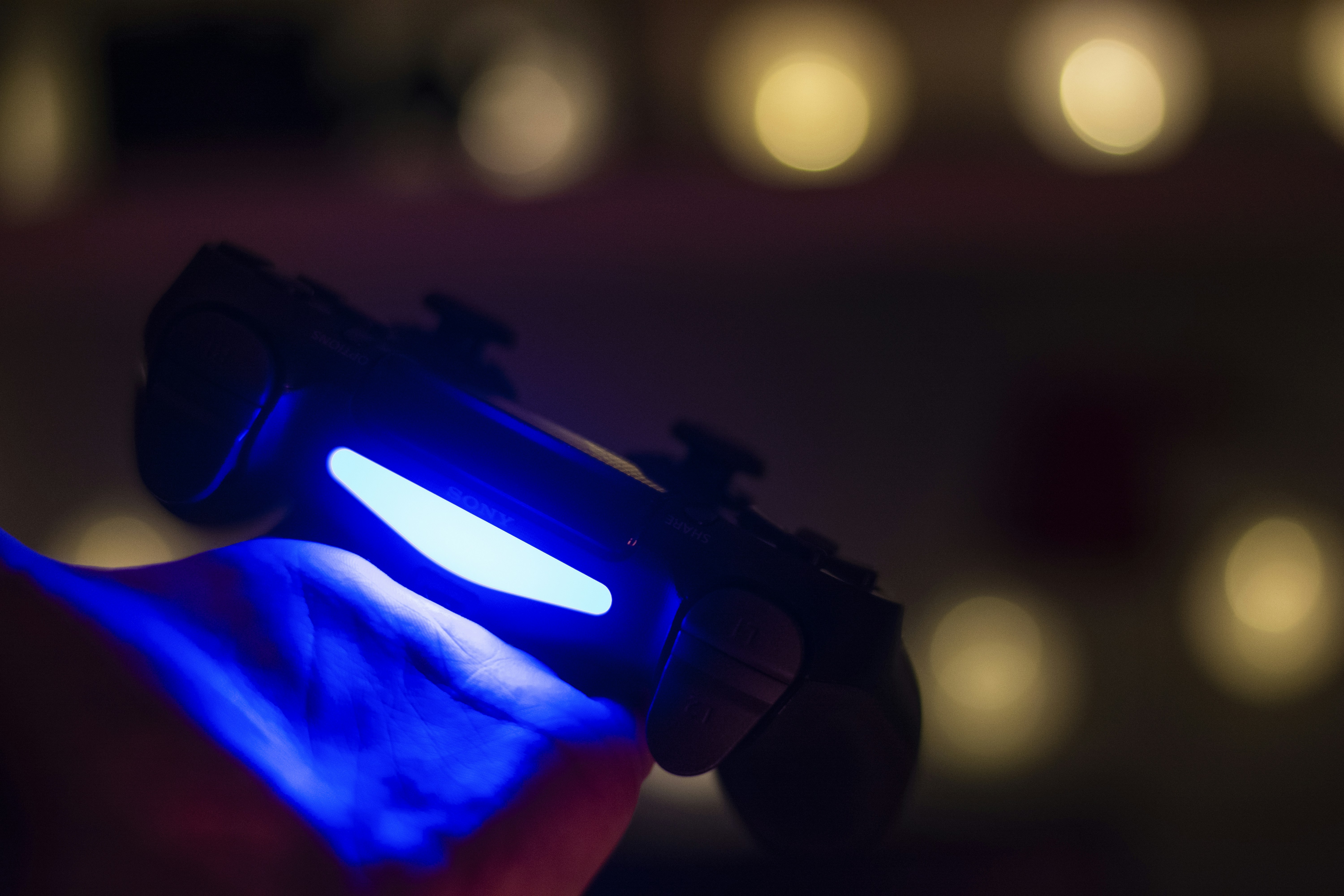 Glowing PlayStation 4 game pad on hand with bokeh background
