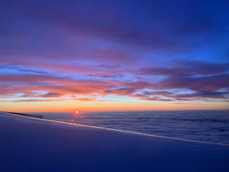 A breathtaking panoramic shot of a vibrant sunset sky blending orange, pink, and purple hues with a silhouette of an airplane soaring.