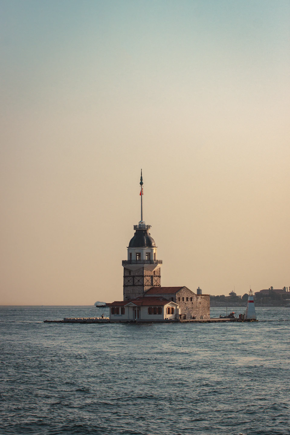 The image depicts a picturesque scene at the Bosphorus strait, featuring the iconic Sultan Ahmed Mosque, also known as the Blue Mosque or the Hagia Sophia, situated on an island amidst the deep blue waters. The mosque is characterized by its distinctive dome and white walls adorned with red tiles. A tall tower stands prominently in the center of the image, reaching towards the sky. In the background, a few boats can be seen floating on the water, adding to the serene atmosphere of the scene.

The perspective of the photo is from across the water, providing a comprehensive view of the mosque and its surroundings. The colors in the image are predominantly blue and white, reflecting the calmness of the sea and the architectural beauty of the mosque.