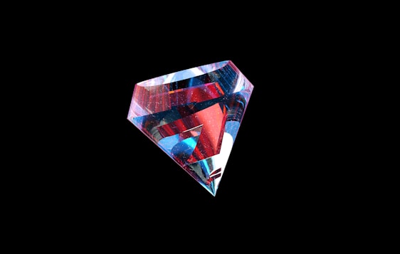 A multifaceted gem with a complex interplay of colors, featuring reflective surfaces that include shades of red, blue, and white. The gem is set against a stark black background, highlighting its vivid color spectrum and intricate geometric shape.