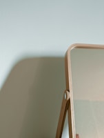 Close-up of a 60 cm round mirror framed in natural wood, reflecting soft sunlight in a modern bedroom