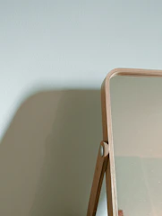 A close-up of a round wall mirror with a thin wooden frame reflecting soft natural light in a minimalist room.