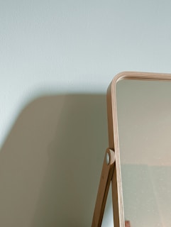 A minimalist mirror framed in wood, reflecting a softly lit bathroom interior.